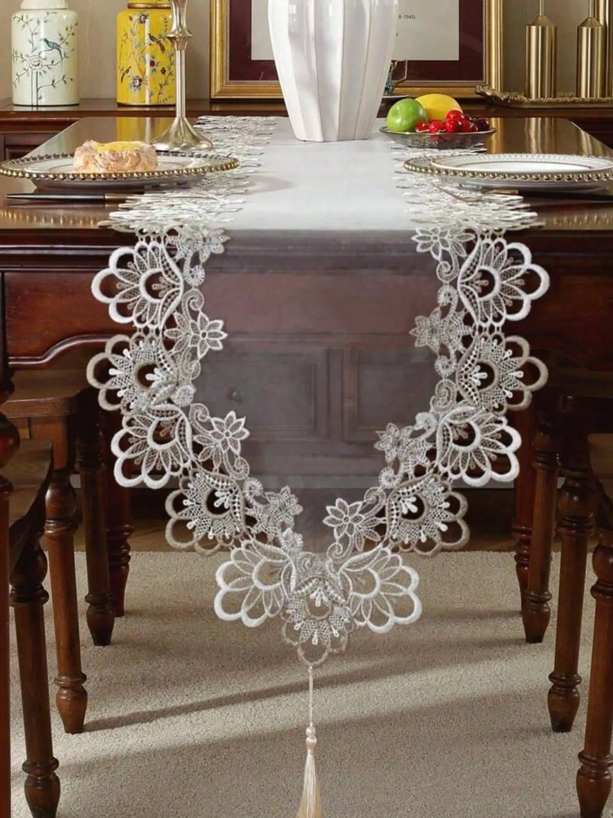 White embroidered mesh lace table runner with decorative pendants displayed on a dark wooden table.