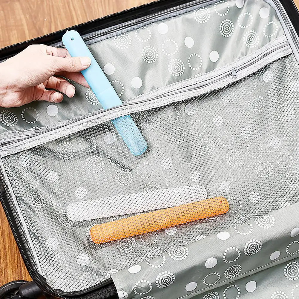 A hand is placing a light blue portable toothbrush into the clear, ventilated cover of a gray travel case.