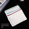 A stack of four white canvas tote bags with colored zippers are displayed on a black surface.
