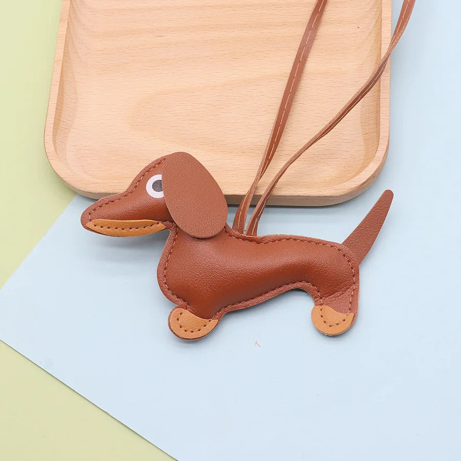 A brown PU leather dachshund puppy keychain with a stitched nose and ear, resting on a light wooden tray.