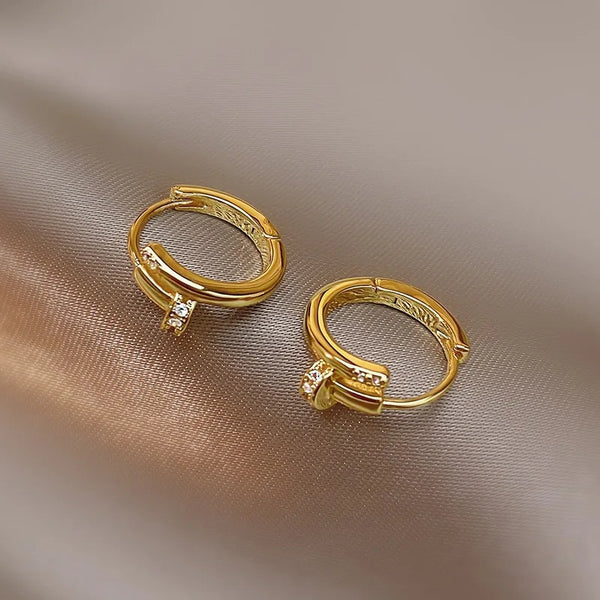 Pendientes de aro dorados con pequeñas cristales transparentes sobre un fondo neutro.