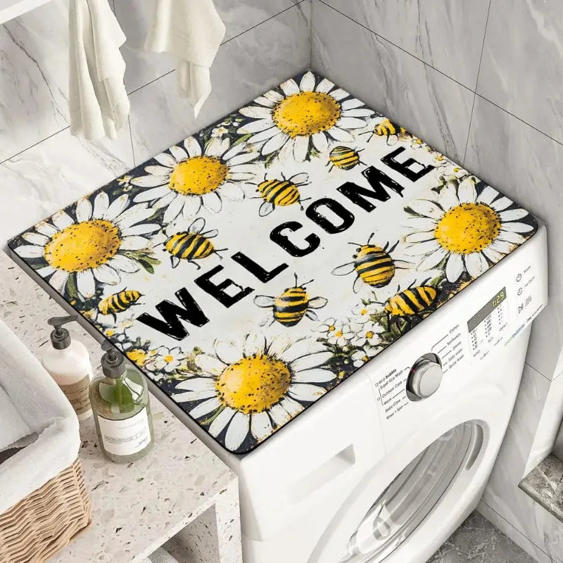 A white washing machine is covered with a floral print absorbent protective mat featuring yellow and black bees and daisies.