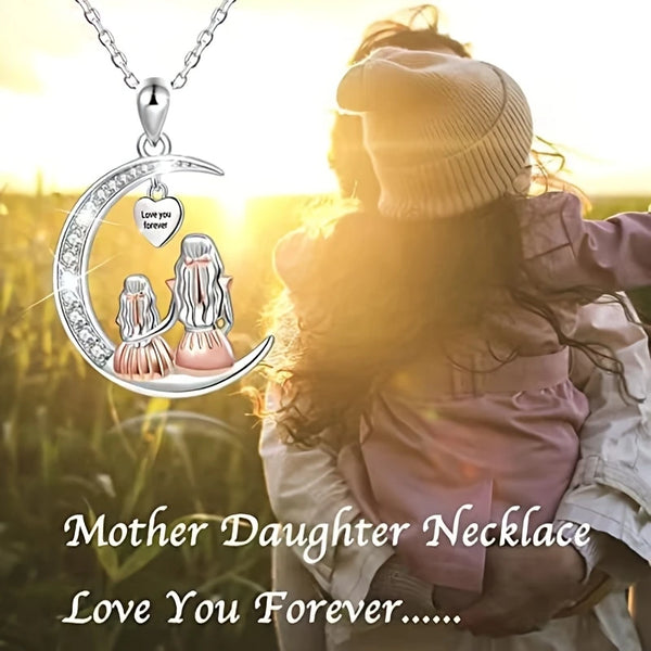 Une femme portant une veste claire tient un collier pendentif de lune représentant une mère et sa fille.