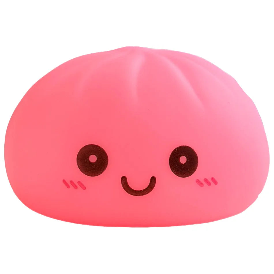 Un juguete rosa y blandito con forma de cara de dumpling sonriente, ojos y mejillas negras.