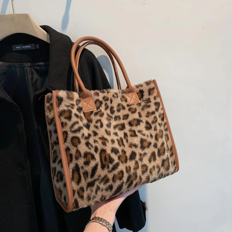 A close-up of a brown faux fur leopard print tote bag being held by a person, displayed next to a black jacket.