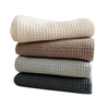 A stack of four waffle weave towels in beige, brown, light gray, and dark gray.