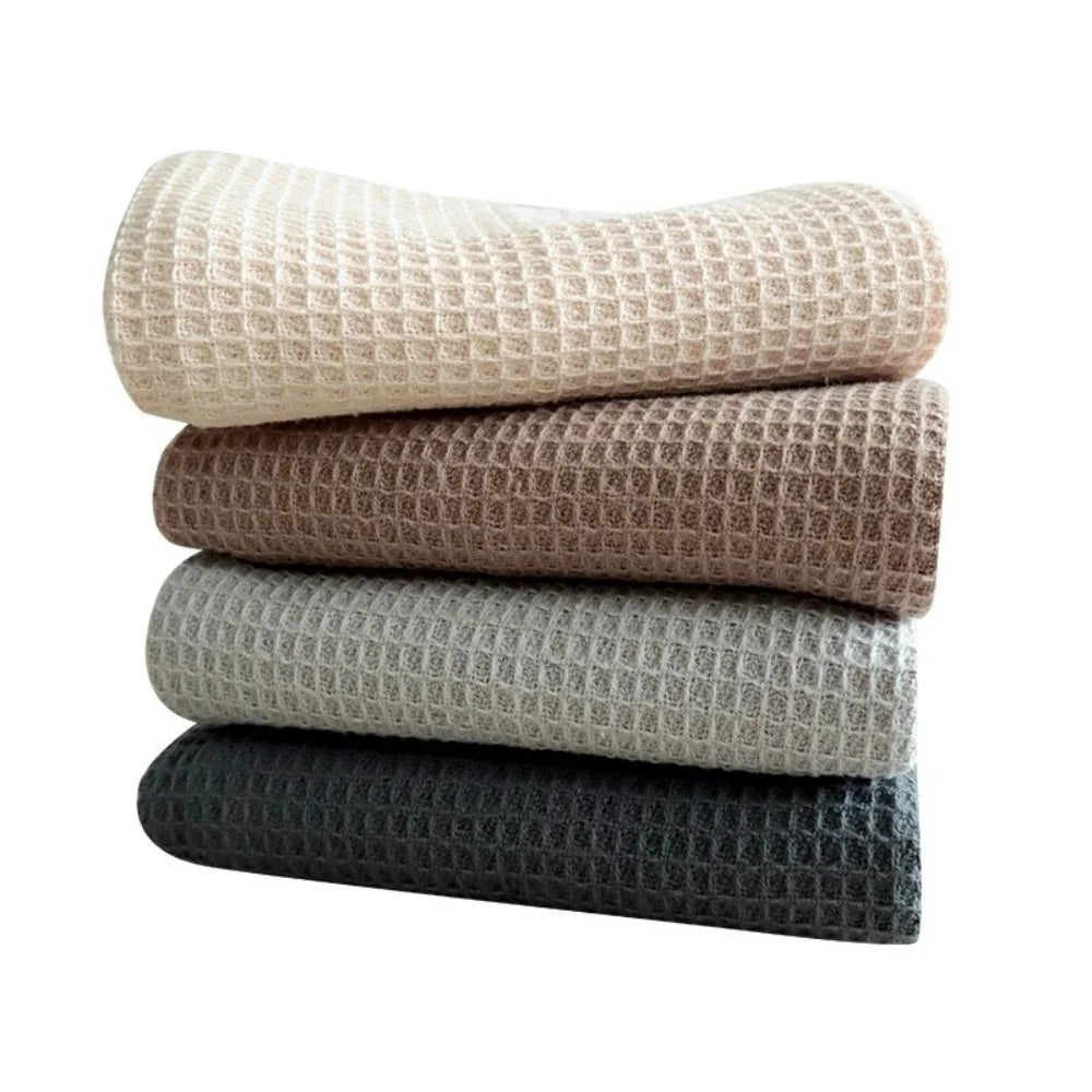 A stack of four waffle weave towels in beige, brown, light gray, and dark gray.