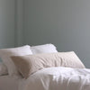 White linen pillowcases and a duvet on a bed against a light gray wall.