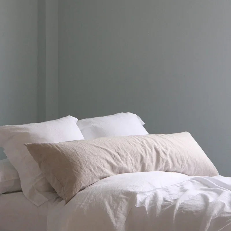 White linen pillowcases and a duvet on a bed against a light gray wall.
