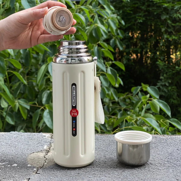 Une main tient une bouteille d'eau isotherme en acier inoxydable à double paroi blanche et son couvercle assorti, avec une ta