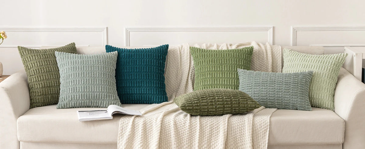 A set of seven textured throw pillows in various shades of green and teal are displayed on a light-colored sofa.