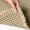 A close-up of a beige waffle weave bath mat with fluffy tassels being held by a hand.