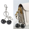 Silber- und Goldkristall-Obstcharm-Schlüsselanhänger an einer hellbeigen Handtasche.