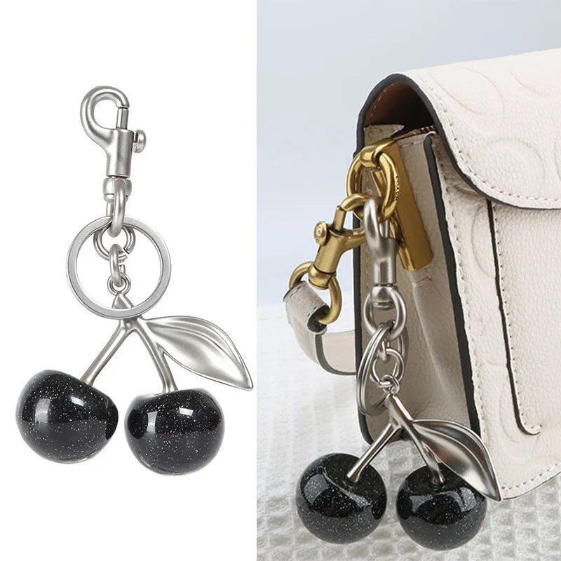 Silber- und Goldkristall-Obstcharm-Schlüsselanhänger an einer hellbeigen Handtasche.