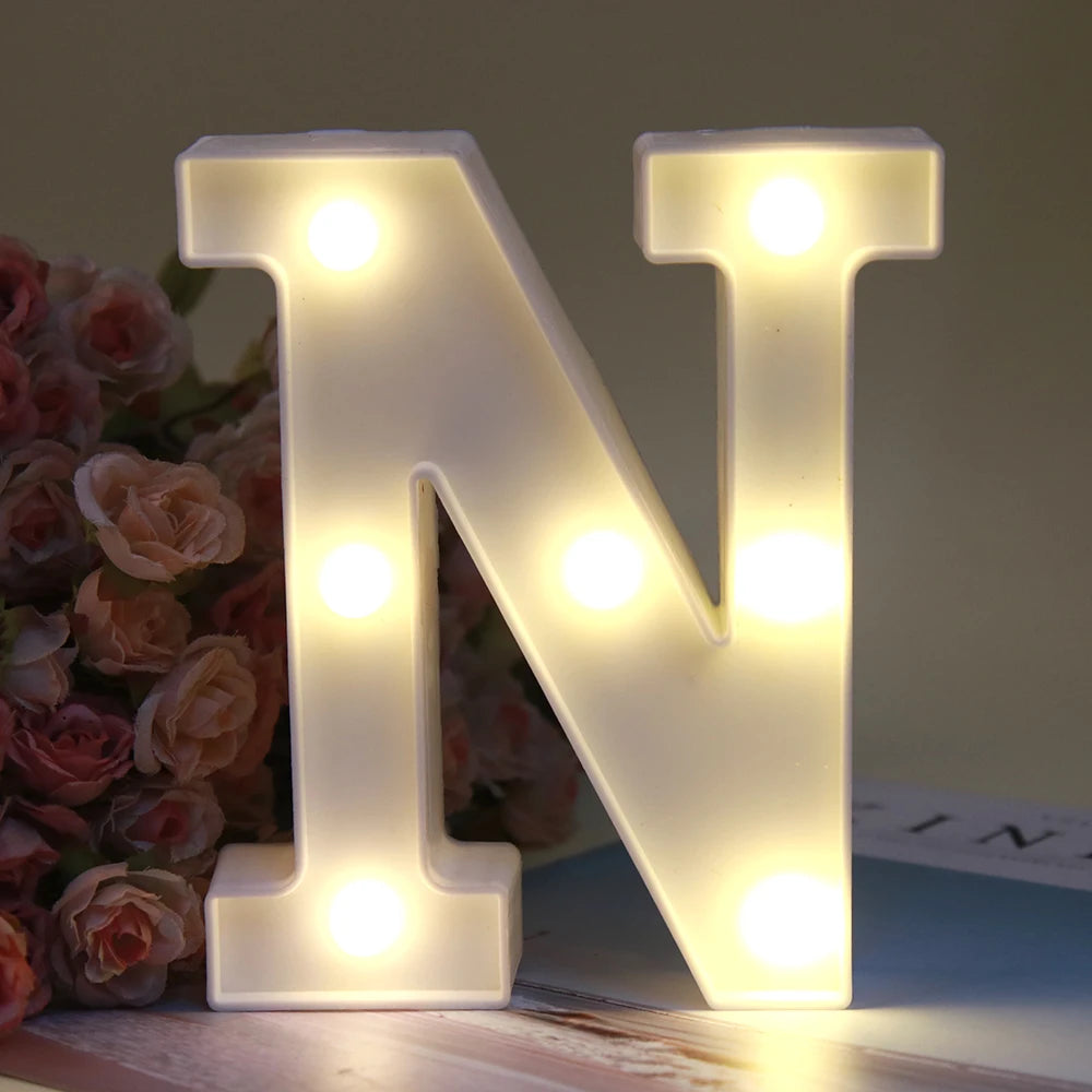 Lettre alphabet N lumineuse blanche LED, veilleuse, posée sur bois à côté de roses roses.