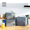 Two grey thermal insulated lunch bags with adjustable shoulder straps resting on a wooden table.