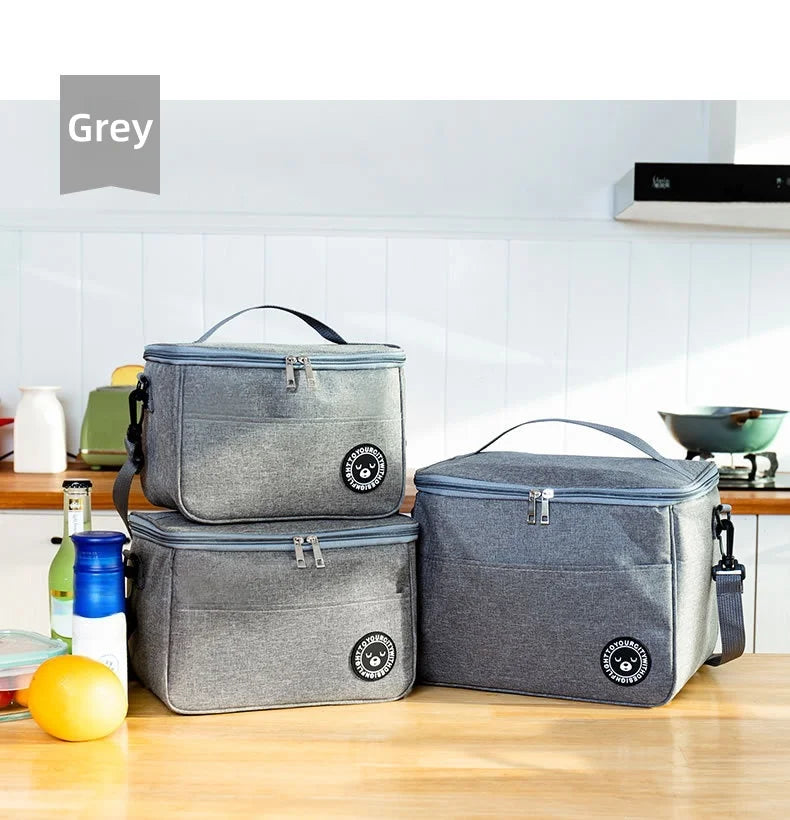Two grey thermal insulated lunch bags with adjustable shoulder straps resting on a wooden table.