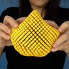 A hand holds a yellow 3D printed articulated starfish fidget toy with a textured, diamond-patterned surface.