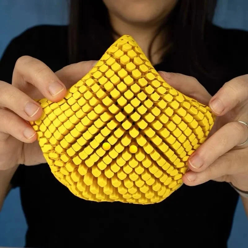 A hand holds a yellow 3D printed articulated starfish fidget toy with a textured, diamond-patterned surface.
