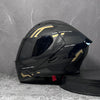 A black modular flip-up motorcycle helmet with gold accents is displayed on a dark surface.