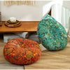 A vibrant teal and green bohemian cotton linen floor cushion resting on a wooden table next to an orange patterned cushion.