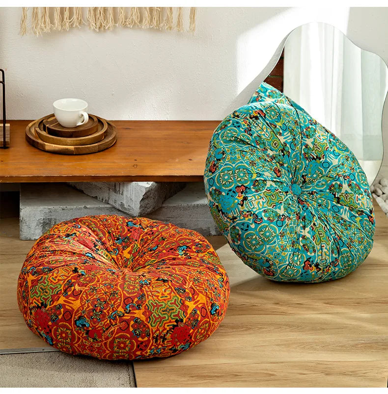 A vibrant teal and green bohemian cotton linen floor cushion resting on a wooden table next to an orange patterned cushion.