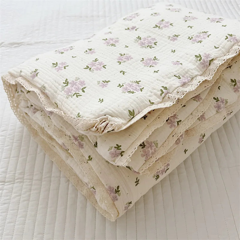 A stack of floral muslin baby blankets in cream and lavender tones folded on a white surface.