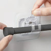 A hand is installing adhesive curtain rod hooks onto a clear plastic wall mount clip for a no-drill installation.