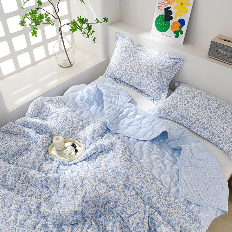 Light blue floral quilted blanket with matching pillows displayed on a white shelf.