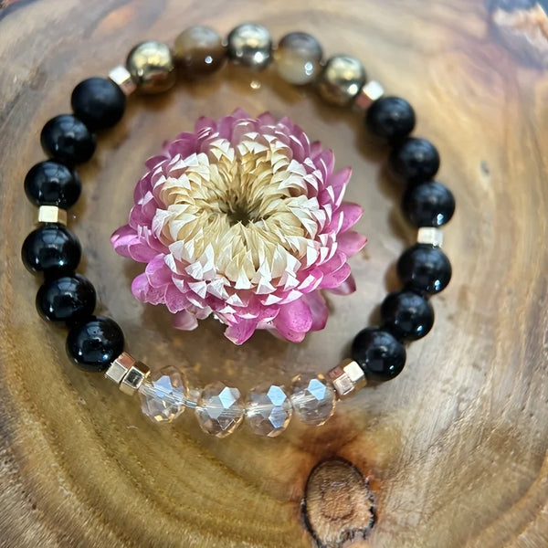 Bracelet en perles noires et dorées avec une grande fleur rose, exposé sur une surface en bois.
