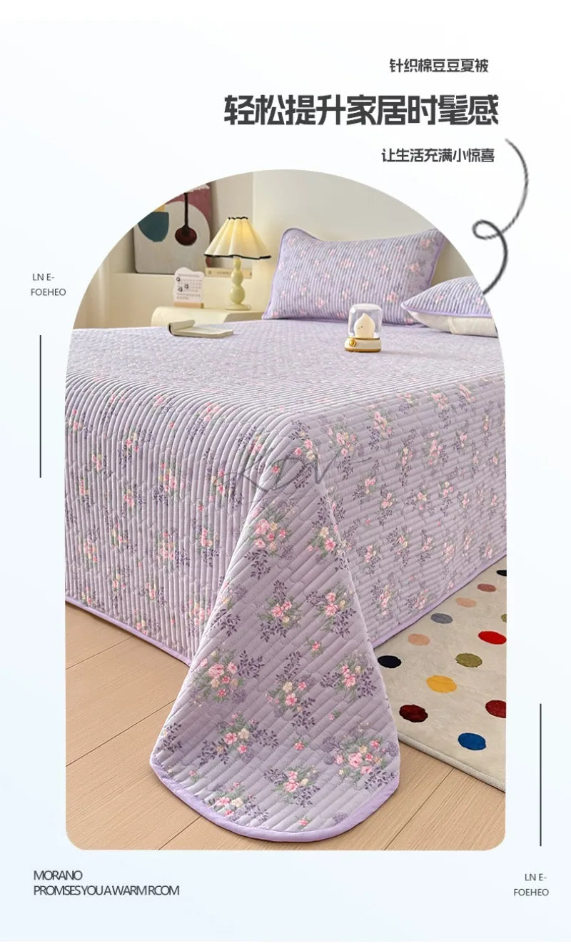A lilac floral quilted bedspread draped on a bed, emphasizing its dust-proof feature.