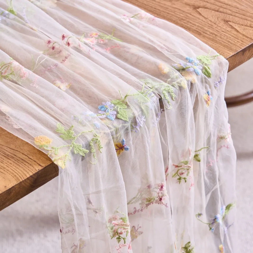 Sheer pink tulle table runner featuring delicate floral embroidery on a wooden table.