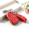 A red TPU smart key fob cover with a silver keychain attached, resting on a white surface next to a book.