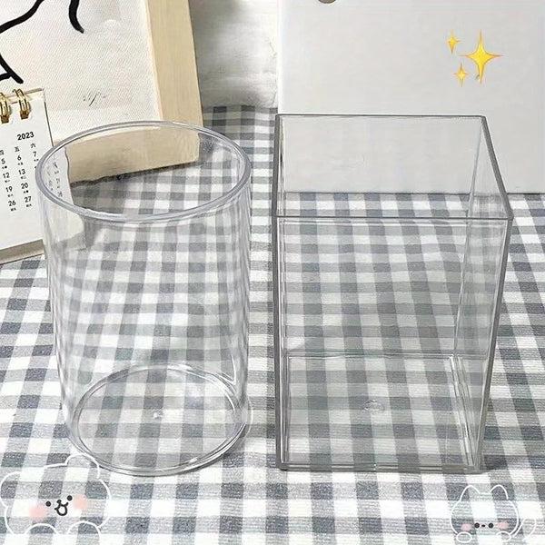 Ein durchsichtiger Acryl-Stifthalter neben einer rechteckigen transparenten Acryl-Aufbewahrungsbox auf einem karierten Stoff.