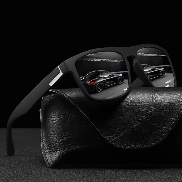 A pair of vintage square sunglasses resting on a black leather surface with a blurred car in the background.