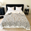 A white leopard print plush jacquard throw blanket draped over a bed with white pillows.