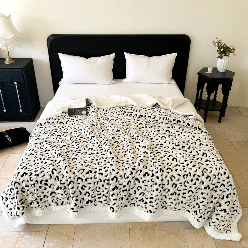 A white leopard print plush jacquard throw blanket draped over a bed with white pillows.