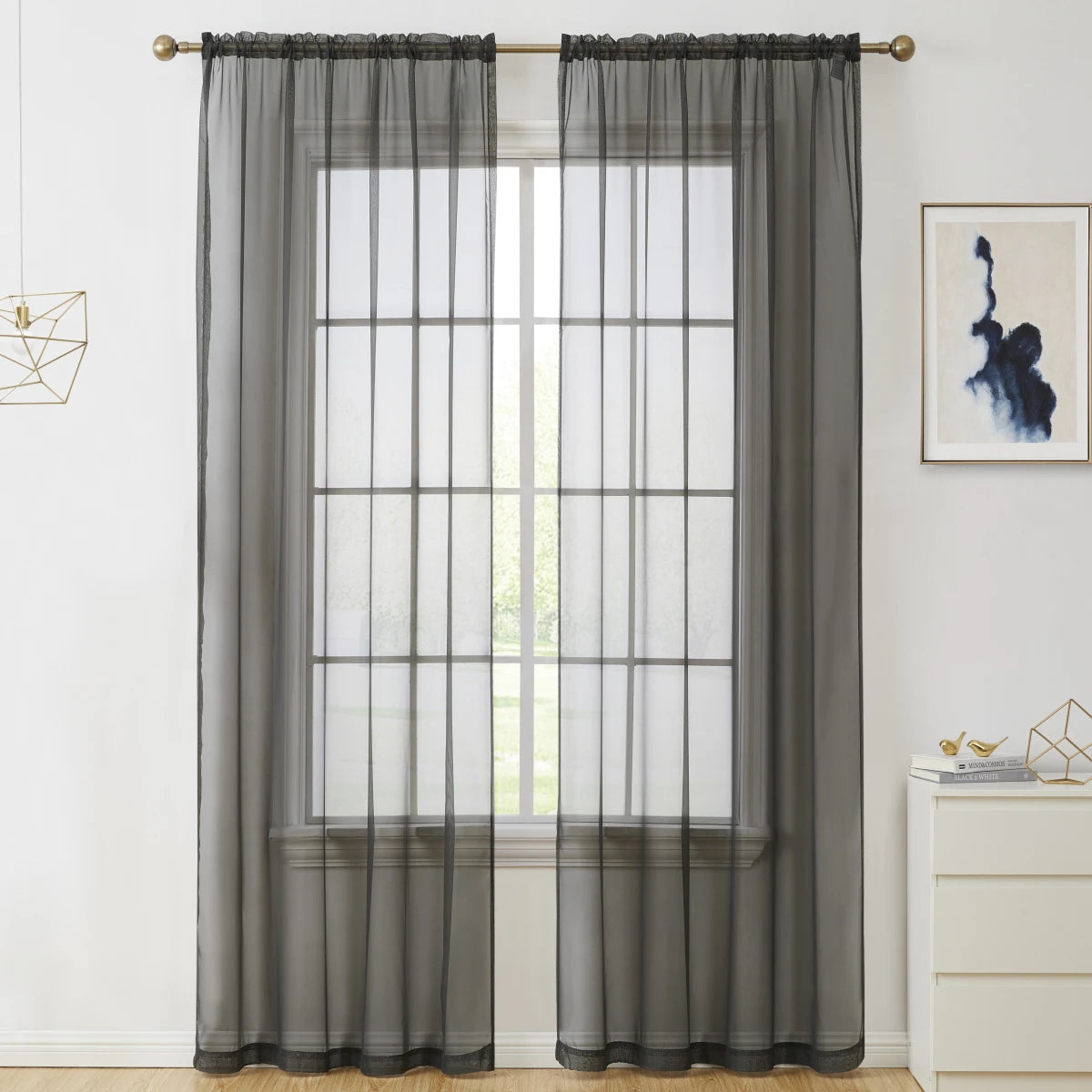 Two panels of sheer gray voile curtains hanging on a rod over a window.