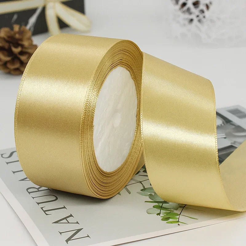 A roll of golden satin ribbon used for gift wrapping or DIY crafts, lying next to a piece of paper.
