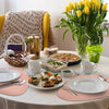 A table setting featuring a meal and tea, surrounded by beige placemats on a white tablecloth.