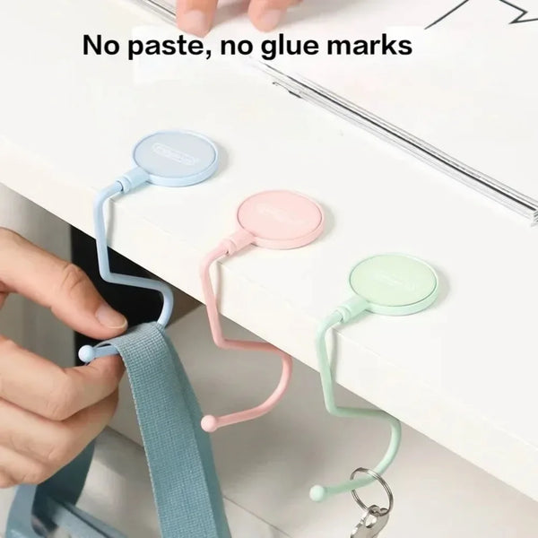 A hand is attaching a silicone hook to a white table edge, demonstrating no paste or glue marks.