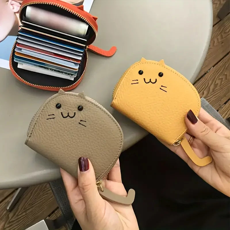 A hand holds a tan cartoon cat-shaped PU leather card wallet next to an open orange zippered case.