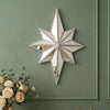 A silver octagonal star resin wall mirror with a distressed finish mounted on a sage green painted wall.