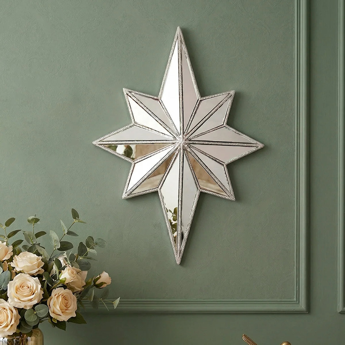 A silver octagonal star resin wall mirror with a distressed finish mounted on a sage green painted wall.