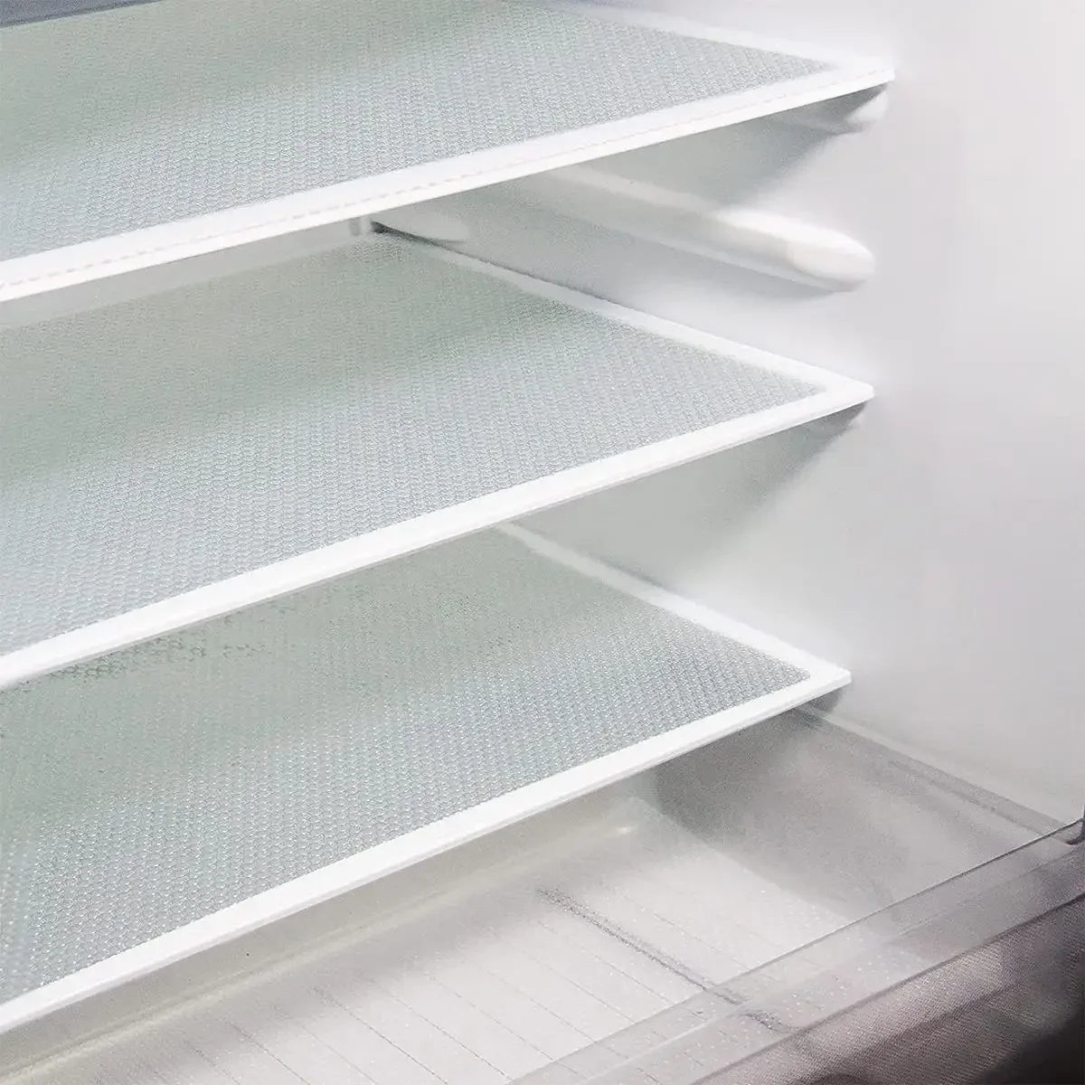A close-up view of three white, textured shelf liners installed inside a refrigerator, showing the interior shelving.