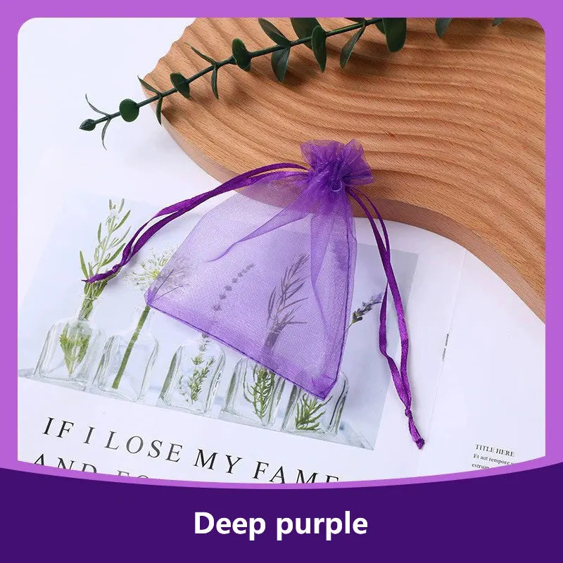 A deep purple organza drawstring gift bag with dried greenery is displayed on a wooden surface.