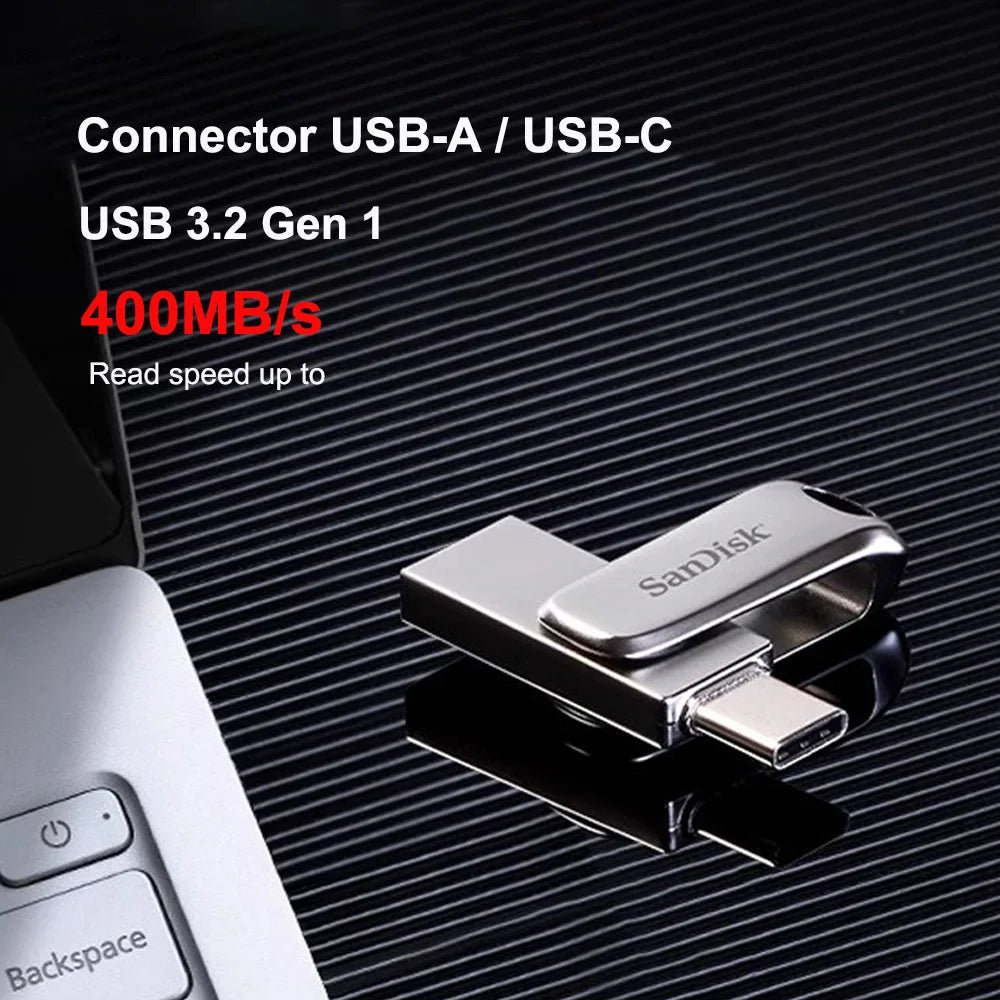 Silver SanDisk Ultra Dual Drive Luxe USB 3.2 flash drive shown on a black background next to a laptop.