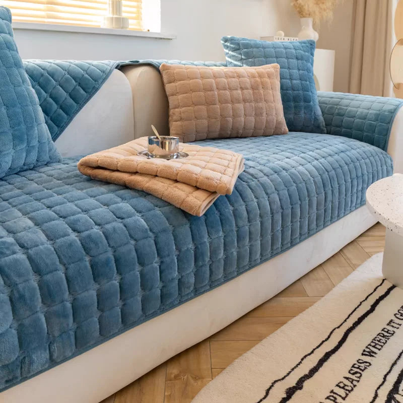 A teal velvet sofa cushion cover with quilted texture and a beige throw pillow on a light-colored sofa.