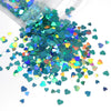 A pile of shiny holographic star sequins in various shades of green, blue, and pink scattered on a white surface.