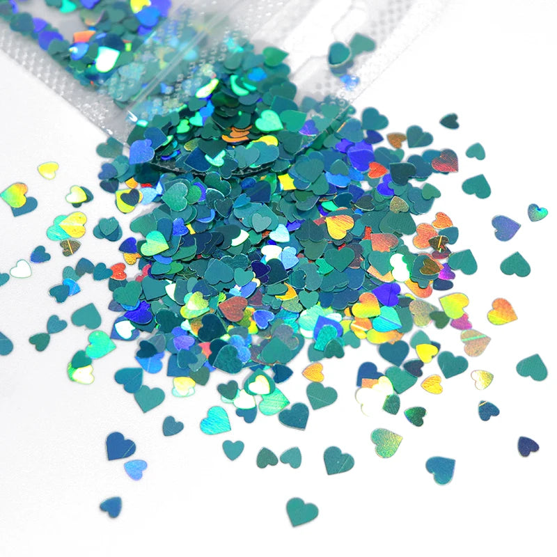 A pile of shiny holographic star sequins in various shades of green, blue, and pink scattered on a white surface.